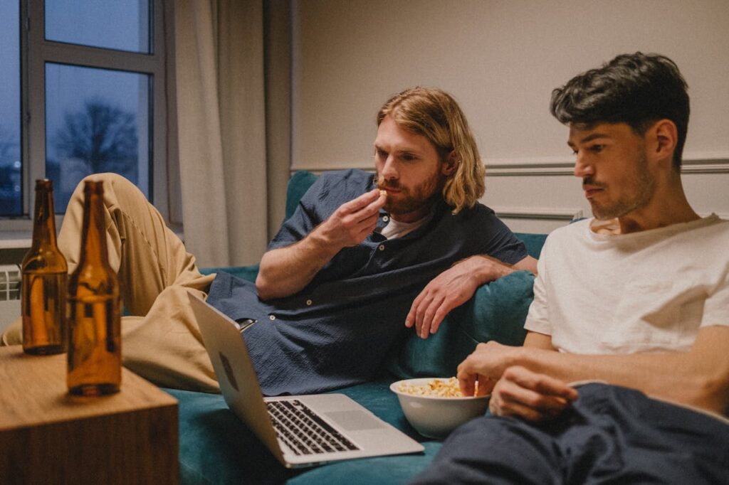 pexels-photo-9627162 Two friends relaxing at home watching a laptop, enjoying snacks and drinks.